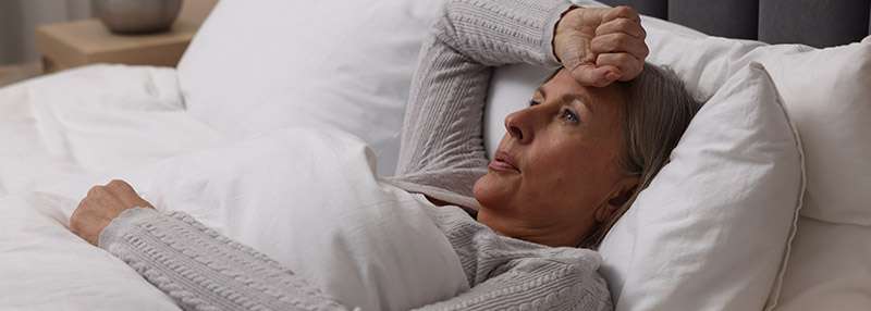 Eine nachdenkliche ältere Frau liegt im Bett und stützt ihren Kopf mit der Hand auf.