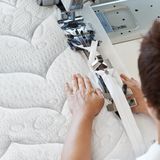 Person sewing on a mattress with a sewing machine, the textured surface is clearly visible.