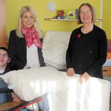 Three people in a room, one in a wheelchair, two standing nearby with pillows and mattresses.
