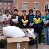 Group of women outdoors holding heart-shaped cushions, with a box and large cushion filling in the foreground.