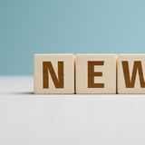 Wooden letters spell "NEWS" on a light table against a blue background.