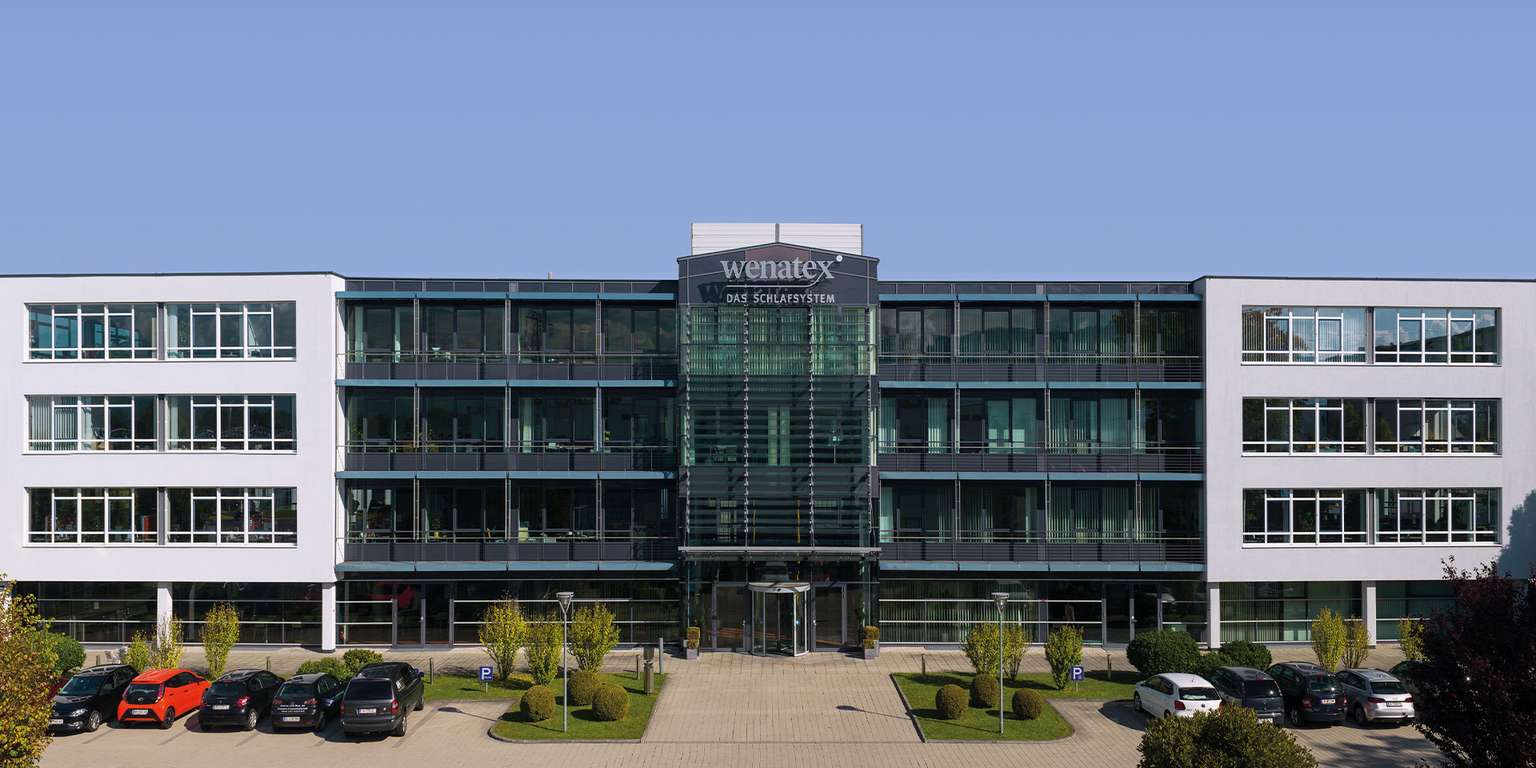 Modern office buildings with glass facades and parking, surrounded by trees and green spaces.