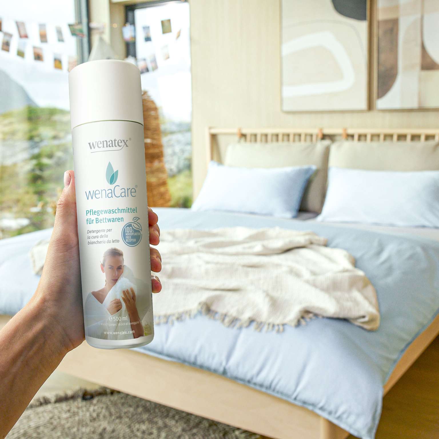 Hand hält Wenatex Pflegewaschmittel für Bettwaren vor einem Schlafzimmer mit Bett und Decke.