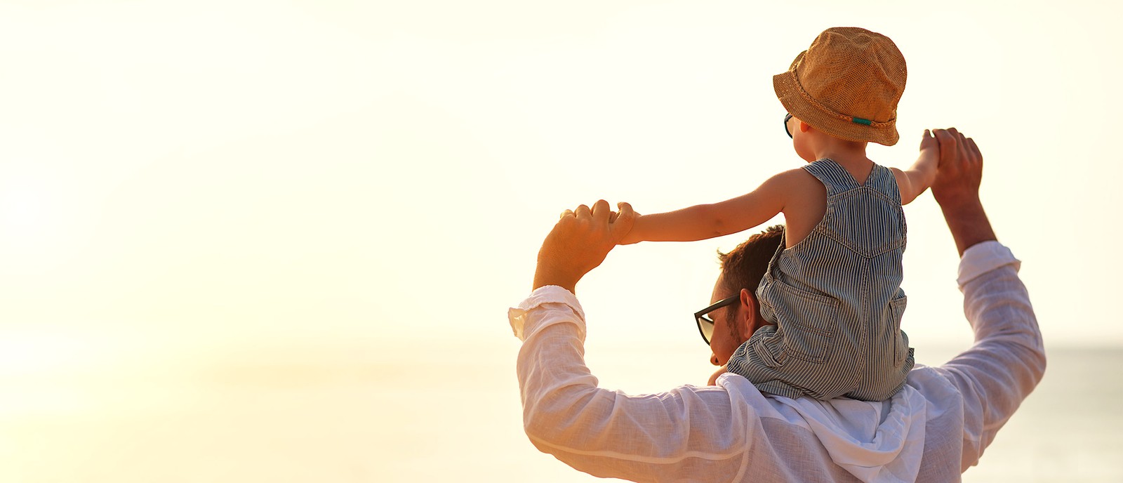 Padre porta il bambino sulle spalle sulla spiaggia, tramonto sullo sfondo, atmosfera rilassata.