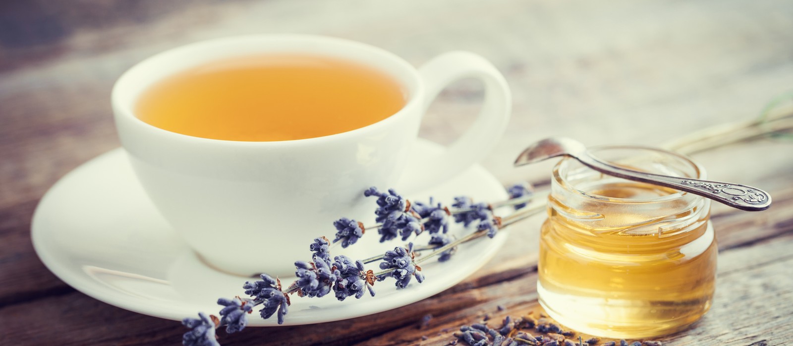 Tazza con tè alle erbe, barattolo di miele e fiori di lavanda su un tavolo di legno.