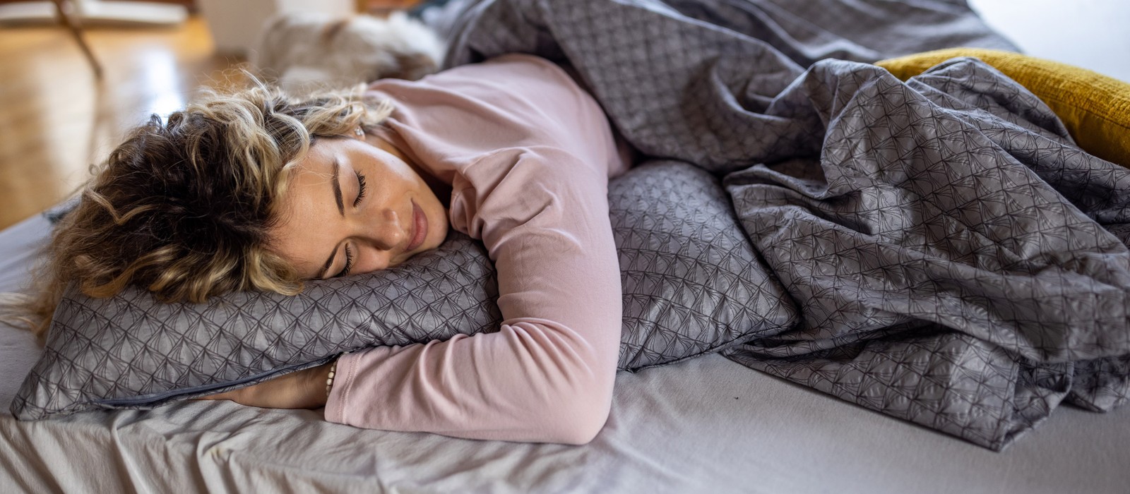 Frau schläft entspannt auf einem Bett mit weichen Kissen und Bettwaren in einem gemütlichen Schlafzimmer.