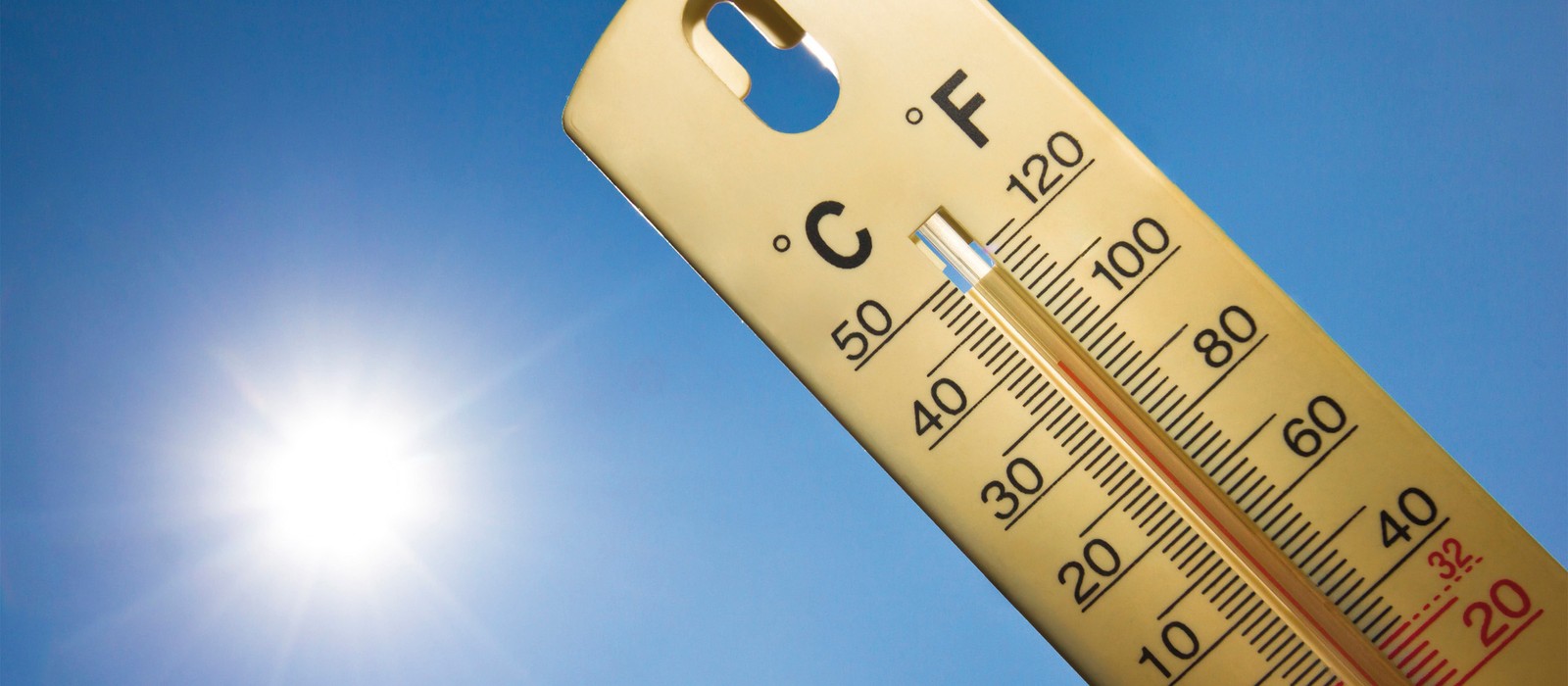 Il termometro mostra alte temperature sotto un cielo blu chiaro con luce solare.