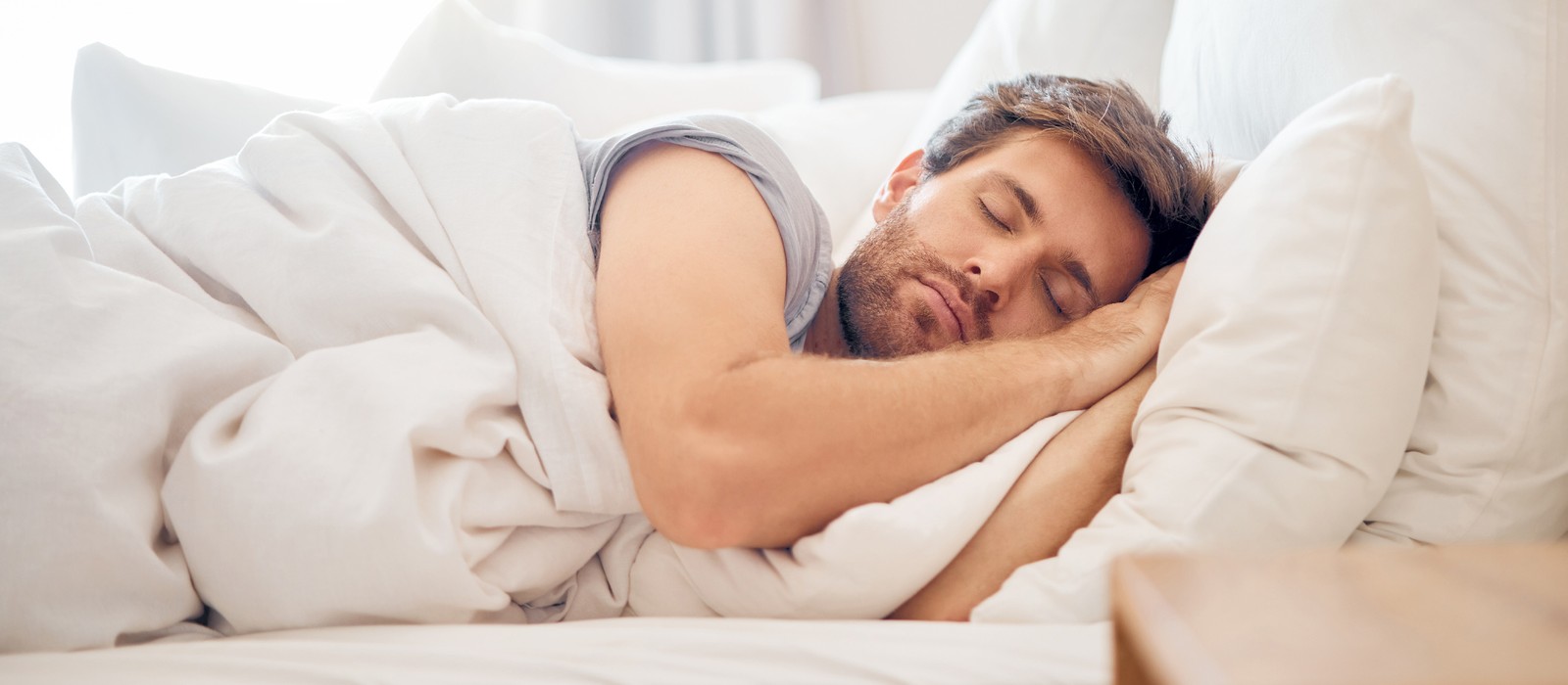 Mann schläft entspannt in einem Bett mit weißen Bettwaren und Kissen.