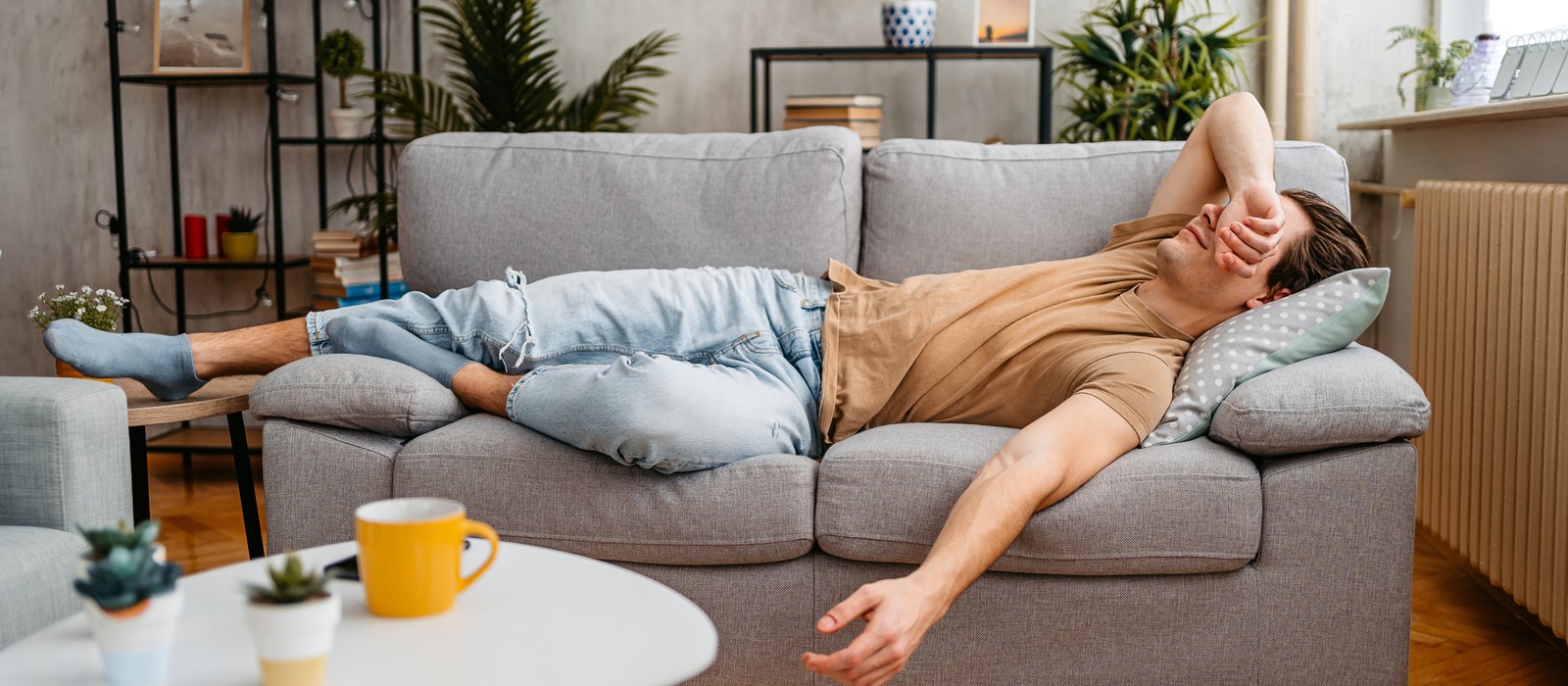 Mann liegt entspannt auf einer Couch, mit einem Kissen unter dem Kopf und einer Hand im Gesicht.