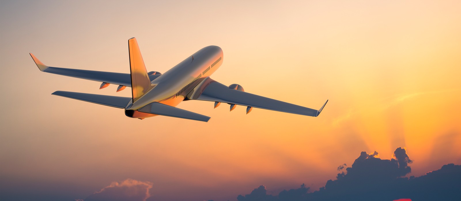 Flugzeug hebt bei Sonnenuntergang in den Himmel ab, umgeben von orangefarbenen und grauen Wolken.