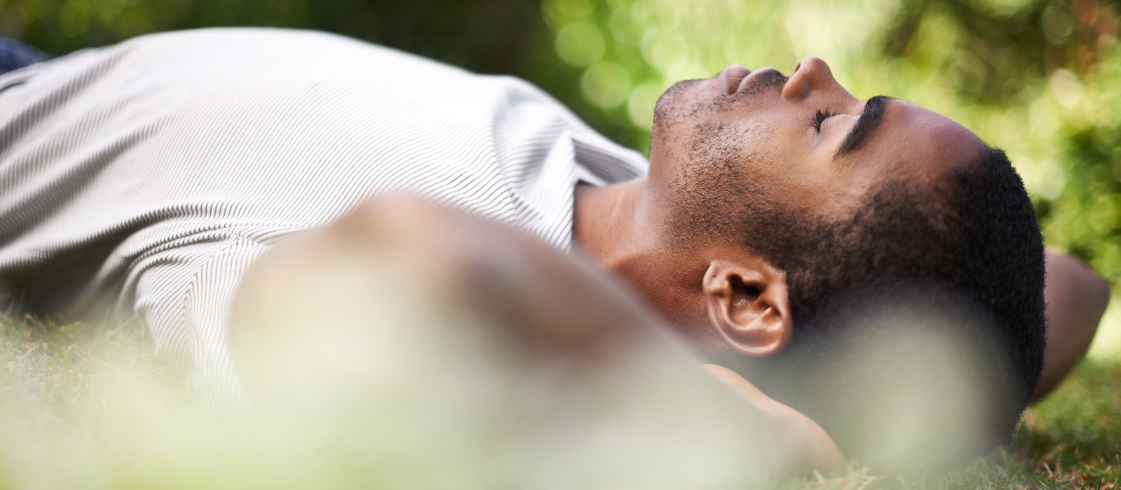 Mann liegt entspannt auf dem Gras und genießt die Natur, mit geschlossenen Augen und Händen hinter dem Kopf.