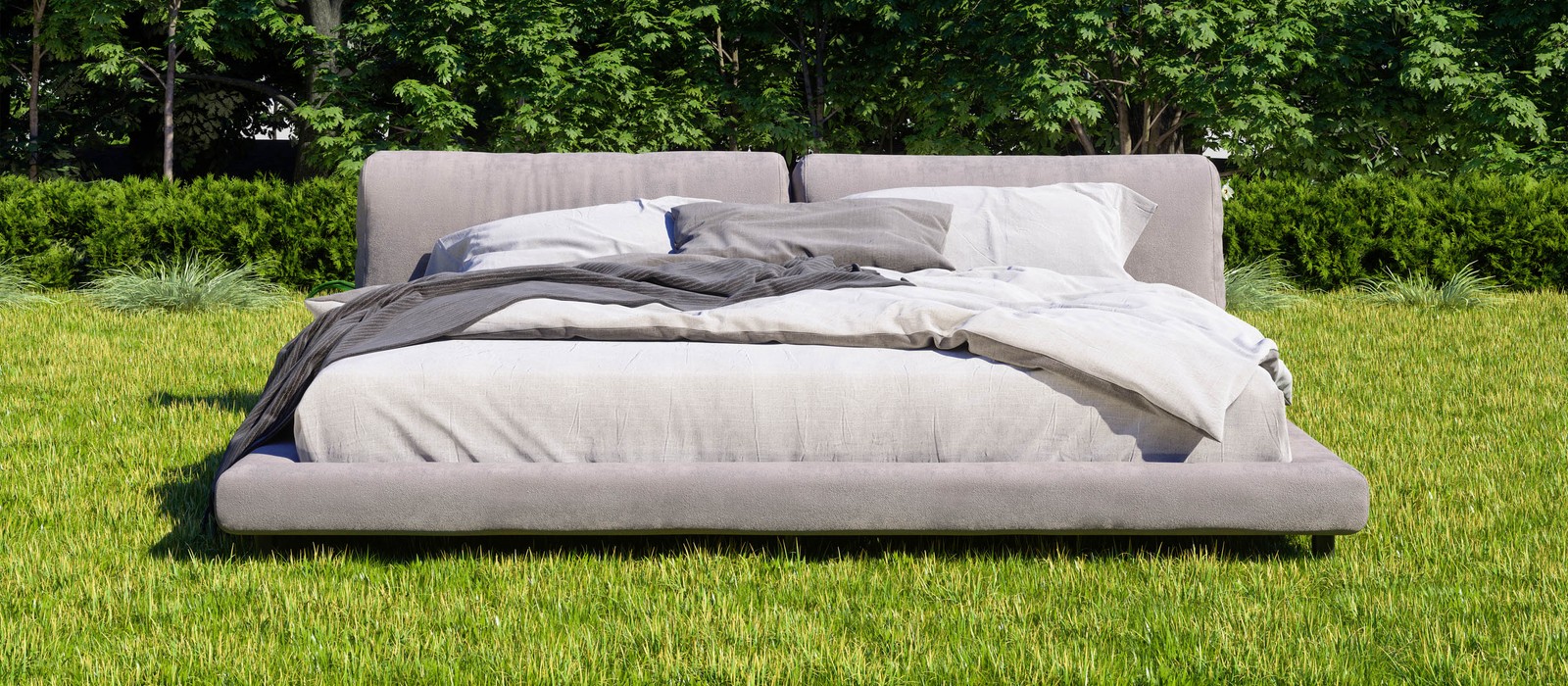 Ein modernes Bett auf einer grünen Wiese, umgeben von Bäumen und Sträuchern.