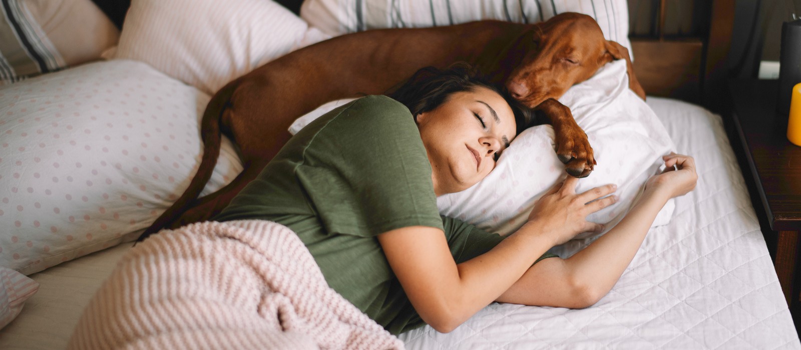 Donna che dorme rilassata a letto, mentre un cane riposa accanto a lei sul cuscino.
