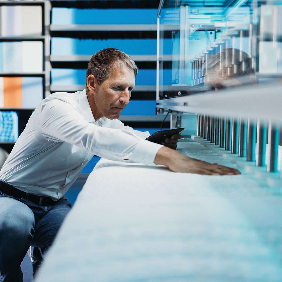 Uomo esamina un materasso in un moderno laboratorio di test con vari dispositivi.