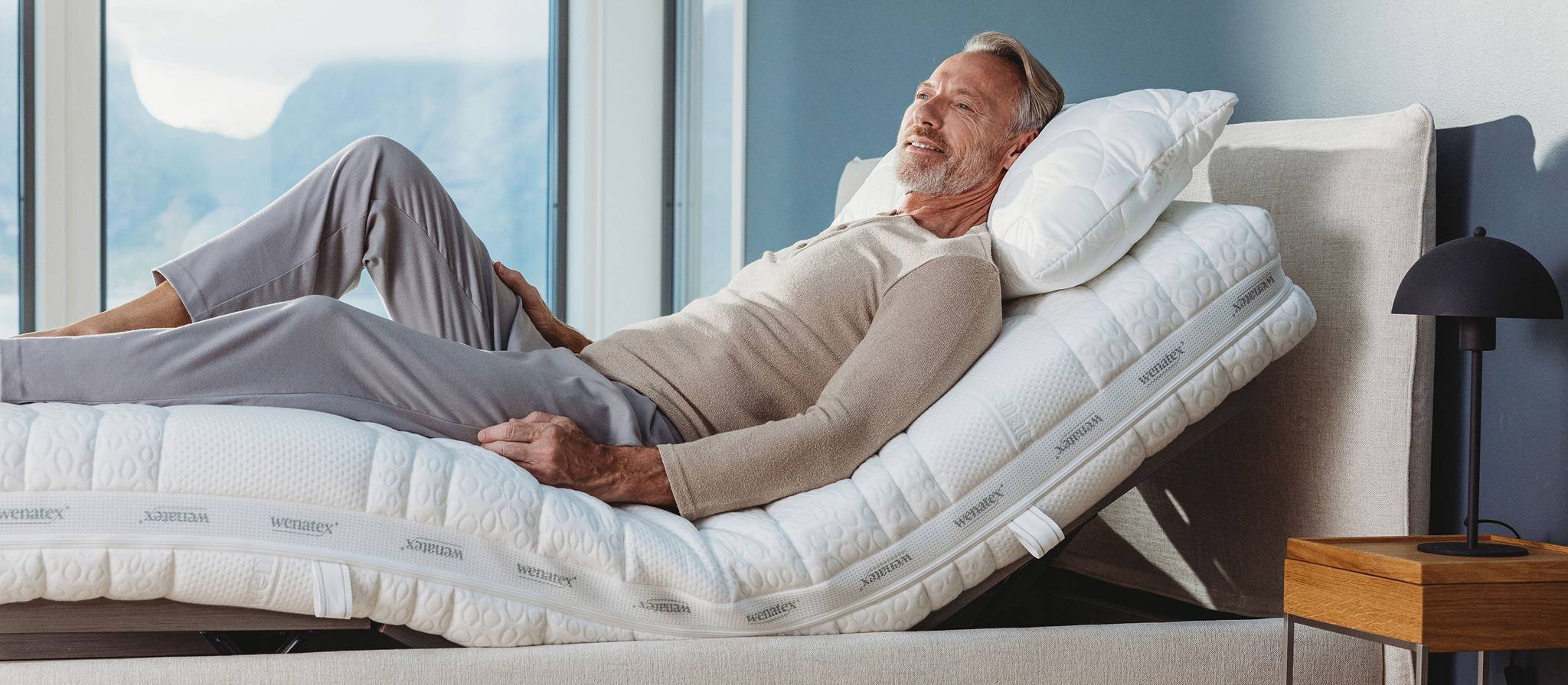Mann entspannt auf verstellbarem Bett mit Matratze und Kopfkissen in modernem Schlafzimmer.