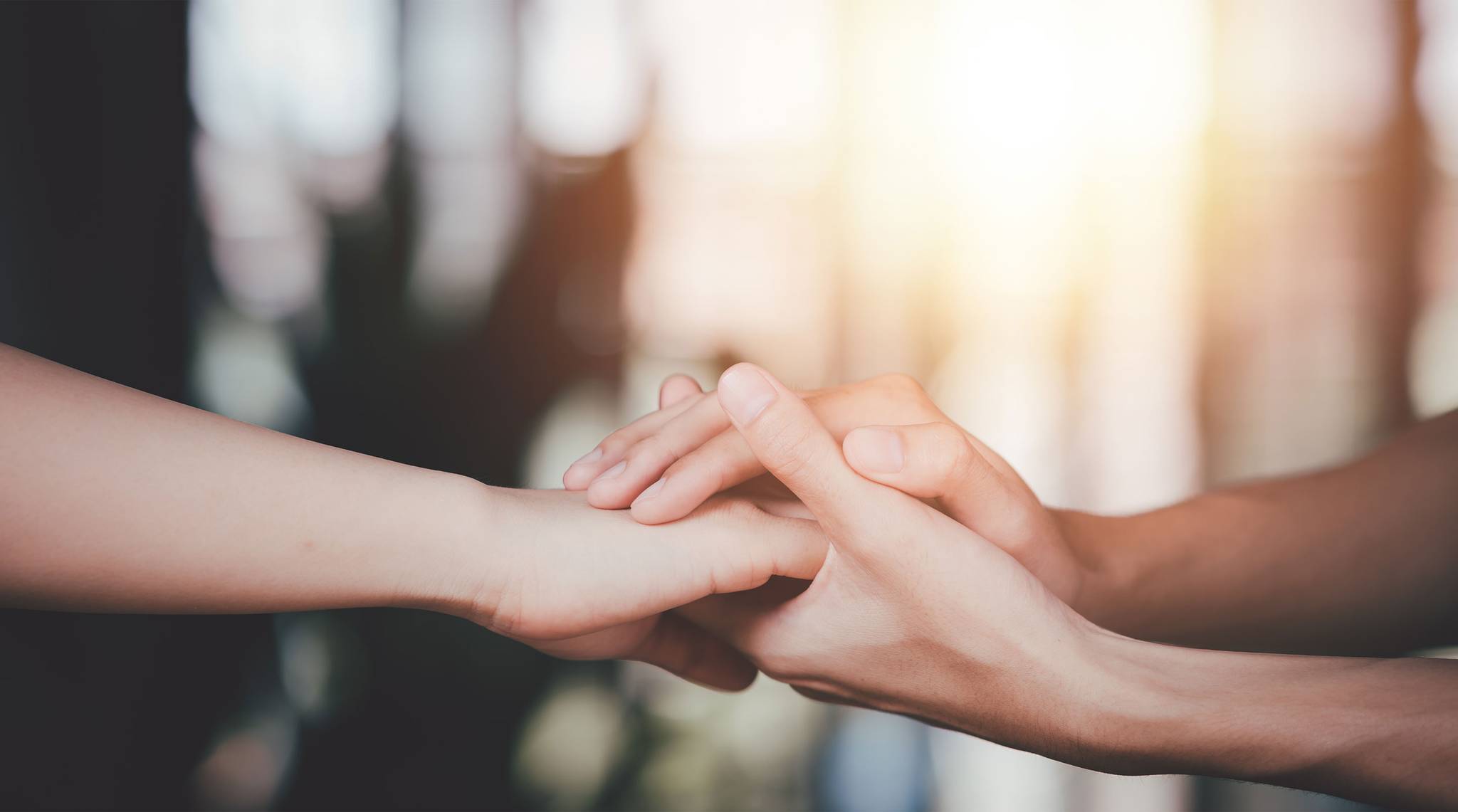 Two hands gently hold each other, symbolizing support and connection in warm light.