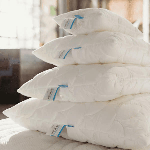 Four stacked white pillows with blue tags on a bed.
