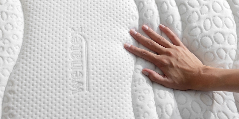Hand berührt die Oberfläche einer Wenatex Matratze mit strukturiertem Bezug.